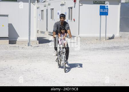 Ein Mann fährt mit einem kleinen Mädchen im Camp in der BLAUEN Zone ein Fahrrad. Innerhalb des neuen Flüchtlingslagers auf der Insel Samos, das mit Unterstützung der EU in Griechenland eingerichtet wurde, ist es die erste von der EU finanzierte geschlossene kontrollierte Einrichtung, das neue Samos RIC (Reception and Identification Center) Da Europa 276 Millionen Euro EU-Mittel für neue Camps auf den Inseln Samos, Lesbos, Chios, Kos und Leros ausgeben wird. Tägliches Leben im neuen Migrantenlager mit den Fertighäusern, einer geschlossenen kontrollierten Einrichtung, in die Menschen nur mit ihrer Karte zusätzlich zu ihrem biometrischen Fingerabdruck eintreten können. Stockfoto