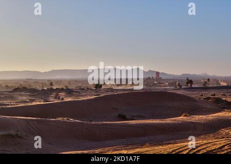 Sanddünen in der Nähe des kleinen Dorfes Merzouga (in der Ferne gesehen) in Marokko, Afrika. Merzouga ist ein Dorf in der Sahara in Marokko, am Rande von Erg Chebbi, einem 50km langen und 5km breiten Sanddünen-Set, das bis zu 350m erreicht. (Foto von Creative Touch Imaging Ltd./NurPhoto) Stockfoto