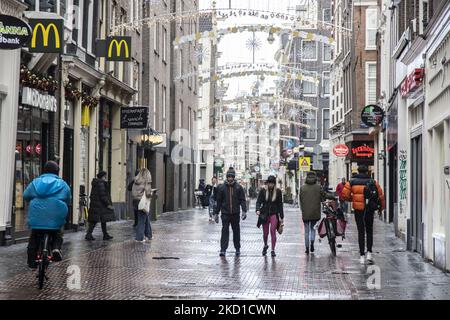 Tägliches Leben während der Sperre bei der vierten Welle der Pandemie. Einheimische und ein paar Touristen in den ruhigen Straßen von Amsterdam während der Sperre in der niederländischen Hauptstadt mit Geschäften und Geschäften, die mit geschlossenen Rollläden aus Metall erscheinen, Cafés, Bars und Restaurants auch geschlossen mit Tischen und Stühlen der Terrassen verschlossen. Die Niederlande waren die erste europäische Nation, die die vollständige Sperre erklärte, um gegen die neue Omicron-Variante zu kämpfen, die aufkommt. Nach einem plötzlichen Regierungsbefehl vor Weihnachten schloss das Land alle unwesentlichen Geschäfte, Cafés, Restaurants, Bars, Fitnessstudios, Schulen, Sport Stockfoto