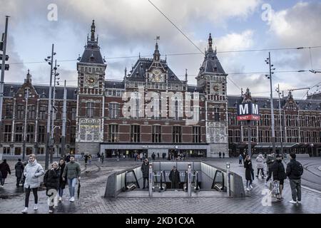 Menschen kommen aus der U-Bahn-Station vor dem Hauptbahnhof Amsterdam Centraal. Tägliches Leben während der Sperre bei der vierten Welle der Pandemie. Einheimische und ein paar Touristen in den ruhigen Straßen von Amsterdam während der Sperre in der niederländischen Hauptstadt mit Geschäften und Geschäften, die mit geschlossenen Rollläden aus Metall erscheinen, Cafés, Bars und Restaurants auch geschlossen mit Tischen und Stühlen der Terrassen verschlossen. Die Niederlande waren die erste europäische Nation, die die vollständige Sperre erklärte, um gegen die neue Omicron-Variante zu kämpfen, die aufkommt. Nach einer plötzlichen Regierung o Stockfoto