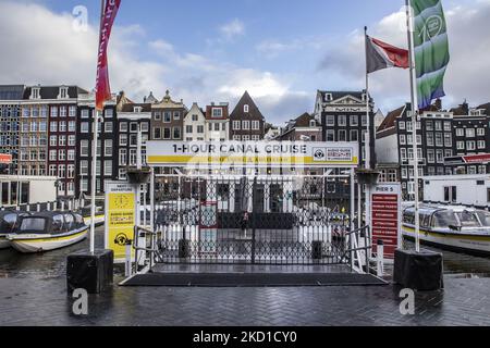 Verschlossene Touristeneinrichtungen für Bootsfahrten und Besichtigungen. Tägliches Leben während der Sperre bei der vierten Welle der Pandemie. Einheimische und ein paar Touristen in den ruhigen Straßen von Amsterdam während der Sperre in der niederländischen Hauptstadt mit Geschäften und Geschäften, die mit geschlossenen Rollläden aus Metall erscheinen, Cafés, Bars und Restaurants auch geschlossen mit Tischen und Stühlen der Terrassen verschlossen. Die Niederlande waren die erste europäische Nation, die die vollständige Sperre erklärte, um gegen die neue Omicron-Variante zu kämpfen, die aufkommt. Nach einem plötzlichen Regierungsbefehl vor Weihnachten schloss das Land alle Nichtessen Stockfoto