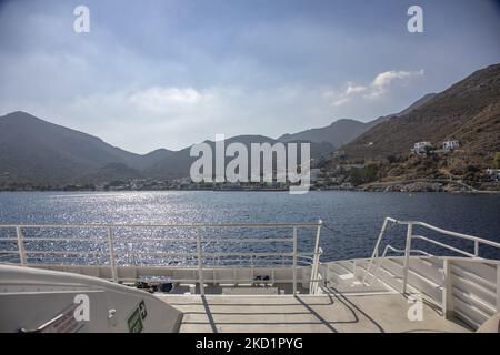 Die Insel Tilos von einer Fähre aus gesehen. Livadia, der Hafen und das Hauptdorf der Insel Tilos mit den weiß getünchten Häusern der traditionellen Architektur und dem Strand mit dem kristallklaren Meerwasser. Telos ist eine kleine griechische Mittelmeerinsel in der Ägäis, einem Teil der dodekanischen Inseln, mit 780 Einwohnern in der Nähe der türkischen Küste. Ende 2018 wurde Tilos die erste Insel im Mittelmeer, die ausschließlich mit Wind- und Solarenergie betrieben wurde, einer grünen autarken Insel, einer von der EU finanzierten Initiative für grüne Energie aus erneuerbaren Quellen zum Schutz der natürlichen Umwelt. Stockfoto