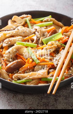 Gebratene Auster- und Shiitake-Pilze mit Karotten, Sesamsamen und grünen Zwiebeln in den Teller auf dem Tisch legen. Vertikal Stockfoto