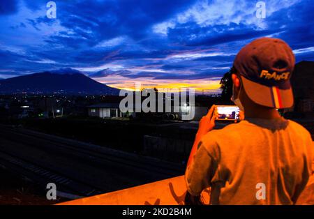 Ein Junge, der am 10. Februar 2022 in Bogor, West-Java, Indonesien, ein Foto vom Blick auf den Mount Salak während des Sonnenuntergangs mit seinem Smartphone machte. (Foto von Adriana Adie/NurPhoto) Stockfoto