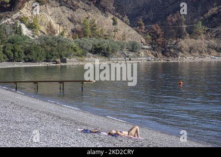 Sonniger Tag und ruhiges Meer am Kohili-Strand, mit Kieselsteinen, während eine Frau die Sonne genießt, in der Nähe des Dorfes Limni, einem Reiseziel, mit dem verbrannten Hang und dem Wald im Hintergrund. Nach den Bränden in Griechenland ereignete sich im Land eine riesige Umweltkatastrophe. An der spezifischen Stelle des Ufers fand im August eine Evakuierung mit einer Fähre statt, als das Feuer das Gebiet umgab. Wald, Pinien, Olivenhaine, Unternehmen, Hotels, Camping, Häuser, Fahrzeuge und Tiere wurden verbrannt. Das Feuer war nach einer Nacht des Regens vorbei, während die vorherigen Tage griechische Feuerwehrleute, lokale Volun Stockfoto