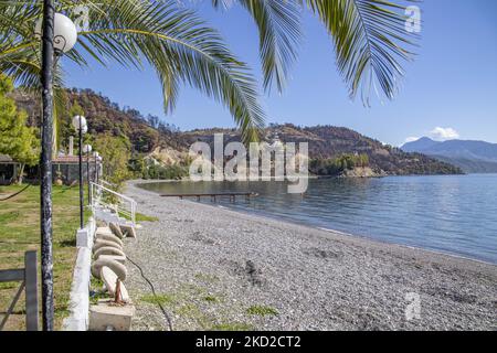 Sonniger Tag und ruhiges Meer am Kohili-Strand, mit Kieselsteinen, während eine Frau die Sonne genießt, in der Nähe des Dorfes Limni, einem Reiseziel, mit dem verbrannten Hang und dem Wald im Hintergrund. Nach den Bränden in Griechenland ereignete sich im Land eine riesige Umweltkatastrophe. An der spezifischen Stelle des Ufers fand im August eine Evakuierung mit einer Fähre statt, als das Feuer das Gebiet umgab. Wald, Pinien, Olivenhaine, Unternehmen, Hotels, Camping, Häuser, Fahrzeuge und Tiere wurden verbrannt. Das Feuer war nach einer Nacht des Regens vorbei, während die vorherigen Tage griechische Feuerwehrleute, lokale Volun Stockfoto