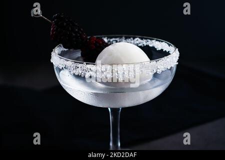 Full Moon Martini mit Blackberry Garnish Side View: Wodka-Cocktail mit einer opaken weißen Eiskugel und Fruchtarnitur Stockfoto