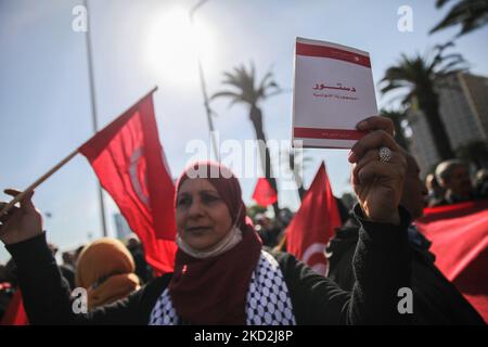 Eine Unterstützerin der islamistisch inspirierten Partei Ennahda hält eine tunesische Flagge, als sie während einer Demonstration auf Initiative der Kampagne „Bürger gegen den Putsch – die Demokratische Initiative“ am 13. Februar auf der Mohamed 5 Avenue in der tunesischen Hauptstadt Tunis eine Kopie der tunesischen Verfassung zeigt. 2022, um gegen die Auflösung des Obersten Justizrats des Landes zu protestieren und die Unabhängigkeit der Justiz zu fordern. Die Demonstranten forderten auch die Freilassung des Vizepräsidenten der Ennahda-Partei Noureddine Bhiri, der seit mehr als sechs Wochen unter Hausarrest gestellt wird. D Stockfoto