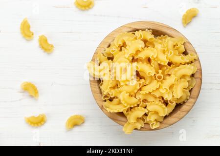 Getrocknete Makkaroni-Jakobsmuscheln. Pasta in einer Holzschüssel und auf einem weißen Tisch. Platz für Text. Stockfoto