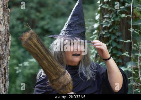 Nahaufnahme einer weißhaarigen Hexe mit Hut und Besen im Waldhintergrund Stockfoto