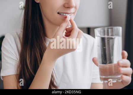 Gesundes Lifestyle-Konzept. Nahaufnahme einer lächelnden attraktiven Frau mit runder Pille und einem Glas Wasser, einer glücklichen jungen kaukasischen Frau, die Ergänzung nimmt, Stockfoto