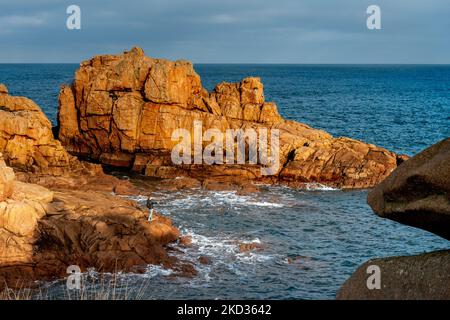 Frankreich, Ploumenach, 2022-01-13. Ein Mann fischt am Ende einer Felsformation entlang der rosafarbenen Granitküste in der Bretagne. Foto von Alexander BEE Stockfoto