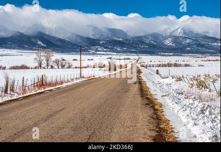 Eine ländliche Landstraße durch schneebedecktes Ranchland führt zu den noch schneebedeckten Bergen der Sangre de Cristo Range in den Colorado Rocky Stockfoto