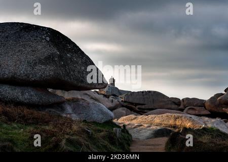 Frankreich, Ploumenach, 2022-01-13. Felsformation entlang der rosafarbenen Granitküste in der Bretagne mit der Spitze des mittleren Ruz Leuchtturms. Foto von Alexand Stockfoto
