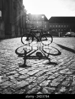 Eine Graustufenaufnahme eines Fahrrads, das geparkt und einen Schatten auf einen Ziegelboden wirft Stockfoto