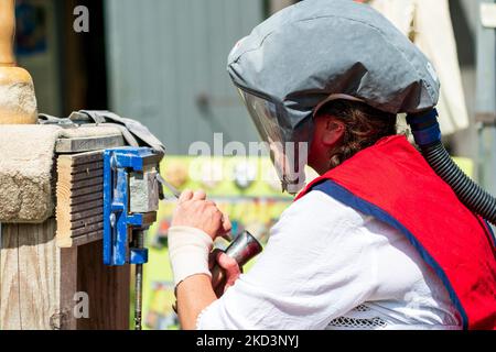 Nahaufnahme einer Frau, die eine schützende Gesichtsmaske mit Luftzufuhr trägt, während sie ein Stück Stein mit Meißel und Hammer modelliert und graviert. Im Freien. Stockfoto