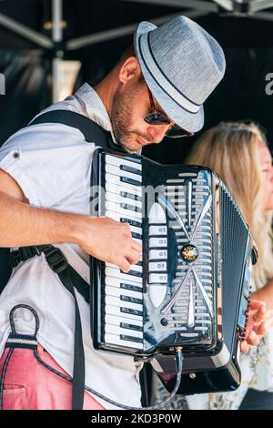 Nahaufnahme eines jungen Mannes mit Hut und Sonnenbrille, der während einer Veranstaltung auf der Bühne auf einer elektrischen Ziehharmonika nach unten blickt. Stockfoto