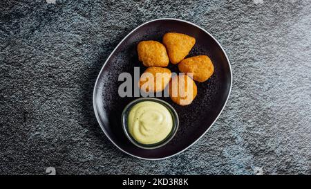 Ein Blick von oben auf goldene Chicken Nuggets mit einer cremigen Sauce auf einem runden Tablett serviert Stockfoto