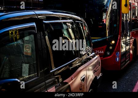 Ein hinteres Taxi und ein roter londoner Bus warten in der Stadt in der Schlange.Reflektionen zeigen eine Fußgängerin, die sich in einem schwarzen Taxi mit starker Hintergrundbeleuchtung widerspiegelt Stockfoto