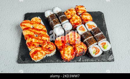 Köstliche, frische Sushi-Brötchen auf einem schwarzen Brett Stockfoto