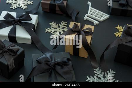Black Friday, Shopping Cart, Weihnachts-Schneeflocke. Verschiedene Geschenkbox mit schwarzem Satinband auf schwarzem Hintergrund, Draufsicht. E-Commerce, Online-Shop-Verkäufe Stockfoto