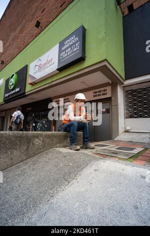 Medellin, Antioquia, Kolumbien - 2 2022. Juni: Bauarbeiter sitzt auf dem Bürgersteig an einem Schild mit der Aufschrift „Verkauf – Mietverträge Stockfoto