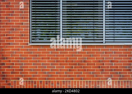 Fragment eines rechteckigen Fensters mit grauen Vorhängen an einer roten Ziegelwand. Aus der „Window of the World“-Serie. Stockfoto