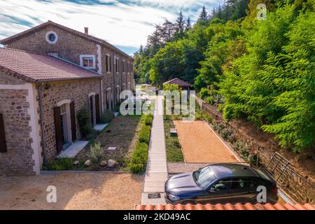 Eine schöne Aufnahme einer großen Steinvilla mit einem Pfad, privatem Garten, schwarzem Auto, Bäumen auf der rechten Seite Stockfoto