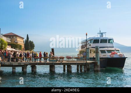 Fähre Gardasee, Blick im Sommer auf die Menschen, die auf dem Fähranleger stehen und auf ein Fährschiff in Gardone Riviera, Lombardei, Italien, warten Stockfoto