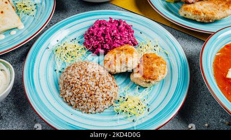 Ein blauer Teller mit Fischkuchen und Buchweizenkörnern mit einer Seite Rote Beete Salat Stockfoto