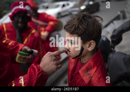 Ein Mann malt das Gesicht eines jungen Jungen mit schwarzer Tinte, als er sich am 12. März 2022 als Hajji Firuz (ein iranisches Neujahrssymbol) auf einer Straße im Norden Teherans tanzt. Hajji Firuz ist eine fiktive Figur in der iranischen Folklore, die zu Beginn von Nowruz auf den Straßen auftaucht. Sein Gesicht ist mit Ruß bedeckt, und er ist in leuchtend rote Kleider gekleidet. Er tanzt durch die Straßen, singt und spielt Musik. (Foto von Morteza Nikoubazl/NurPhoto) Stockfoto