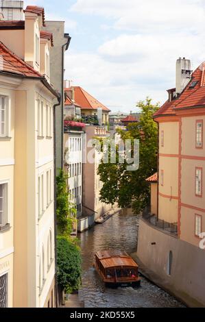 Gebäude mit roten Ziegeldächern. Wenn Sie von der Karlsbrücke in Prag, Tschechien, hinunterblicken, sehen Sie in der Altstadt ein Boot oder einen Lastkahn, das auf dem Wasser schwimmt. Stockfoto