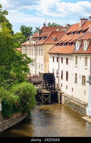 Gebäude mit roten Ziegeldächern. Die Ansicht ist von der Karlsbrücke, Prag, Tschechische Republik, aufgenommen. Sie sehen Fluss oder Kanal mit altem Wasserrad oder Paddelrad. Stockfoto