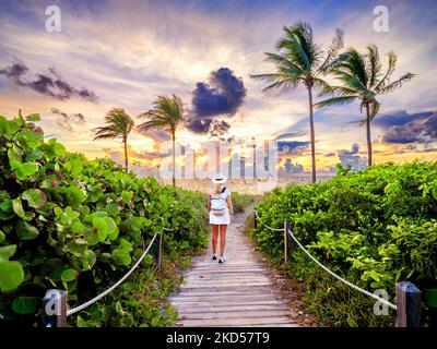 Frau, die auf dem wunderschönen Strandpfad spazieren geht, eingerahmt von Palmen, die zum Strand, Hollywood Beach, Sunrise Miami, South Florida, USA führen Stockfoto