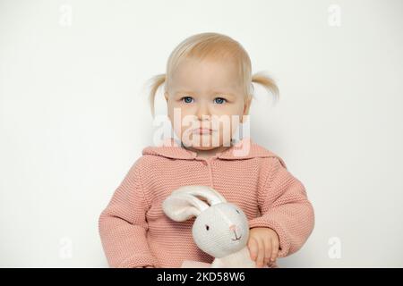 Kleines Mädchen spielen mit ausgestopftem Tier isoliert auf weiß. Kleinkind mit trauriger Gesichtsausdruck und Teddybär. Blonde behaarte Kind in rosa Stockfoto