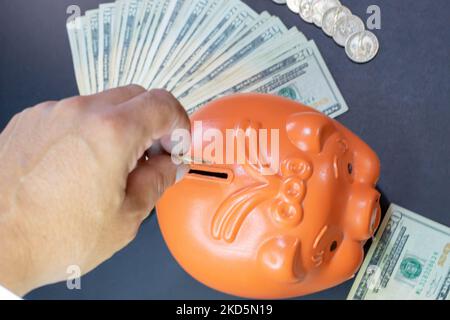 Hand Einzahlung von Münzen in einem Sparschwein. 20-Dollar-Scheine und Münzen. Sparkonzept Stockfoto