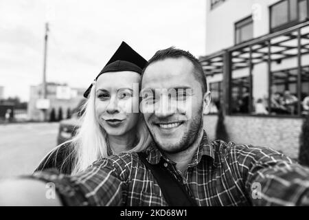 Porträt eines romantischen Paares in Love beim Kamerastudien Selfie-Frau, die bei der Abschlussfeier selbstbewusst schwarze Mütze und einen schwarzen Gatten trägt Stockfoto