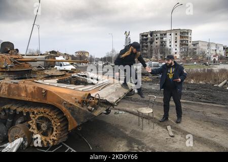 Mann hilft einer Frau, nach einem Foto in der Nähe zerstörter russischer Militärmaschinen in der von der ukrainischen Armee eroberten Stadt Borodyanka in der Nähe von Kiew, Ukraine, 05. April 2022 (Foto: Maxym Marusenko/NurPhoto) Stockfoto