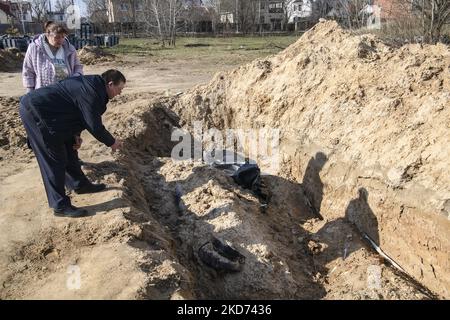 (ANMERKUNG DER REDAKTION: Grafischer Inhalt) Menschen stehen in der Nähe eines Massengrabes, während sie nach Verwandten suchen, die seit dem 15. März vermisst wurden, in der Stadt Bucha, die von der ukrainischen Armee erobert wurde, im Raum Kiew, Ukraine, 07. April 2022 (Foto: Maxym Marusenko/NurPhoto) Stockfoto