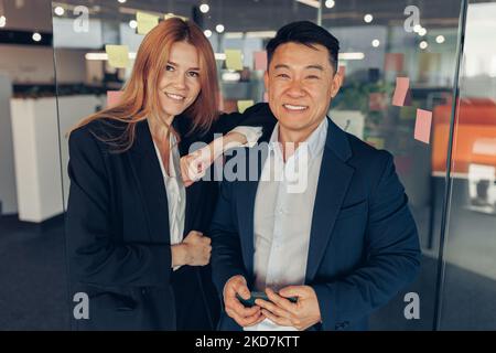 Zwei lächelnde Geschäftsleute, die im Büro zusammenstehen und vor der Kamera stehen Stockfoto