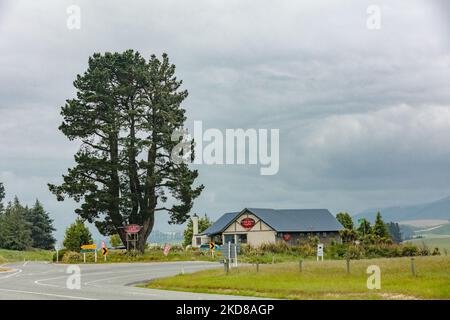 Eine malerische Landschaft mit bewölktem Himmel und einem winzigen Café entlang der Straße zum Lake Tekapo, umgeben von Bäumen Stockfoto