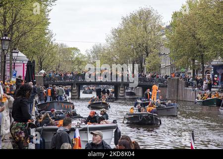 Die Niederlande feiern den Königstag nach zwei Jahren der Annullierung aufgrund der COVID-19 Coronavirus-Pandemie und der Sperrbeschränkungen und -Maßnahmen. Tausende von Einheimischen und Besuchern besuchten die Kanäle von Amsterdam, um mit verschiedenen Festlichkeiten den Geburtstag von König Willem-Alexander, bekannt als Koningsdag, zu feiern, einem niederländischen Nationalfeiertag. Alle Arten von Booten und Schiffen werden in den Kanälen gesehen, die unter den berühmten Brücken und in der Nähe der engen Häuser von Amsterdam vorbeifahren, mit Leuten, die tanzen und Spaß haben. Die Boote ziehen in den Kanälen der Innenstadt entlang, während sich Reisende auf den Straßen versammeln. Du Stockfoto