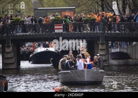 Die Niederlande feiern den Königstag nach zwei Jahren der Annullierung aufgrund der COVID-19 Coronavirus-Pandemie und der Sperrbeschränkungen und -Maßnahmen. Tausende von Einheimischen und Besuchern besuchten die Kanäle von Amsterdam, um mit verschiedenen Festlichkeiten den Geburtstag von König Willem-Alexander, bekannt als Koningsdag, zu feiern, einem niederländischen Nationalfeiertag. Alle Arten von Booten und Schiffen werden in den Kanälen gesehen, die unter den berühmten Brücken und in der Nähe der engen Häuser von Amsterdam vorbeifahren, mit Leuten, die tanzen und Spaß haben. Die Boote ziehen in den Kanälen der Innenstadt entlang, während sich Reisende auf den Straßen versammeln. Du Stockfoto