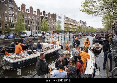 Die Niederlande feiern den Königstag nach zwei Jahren der Annullierung aufgrund der COVID-19 Coronavirus-Pandemie und der Sperrbeschränkungen und -Maßnahmen. Tausende von Einheimischen und Besuchern besuchten die Kanäle von Amsterdam, um mit verschiedenen Festlichkeiten den Geburtstag von König Willem-Alexander, bekannt als Koningsdag, zu feiern, einem niederländischen Nationalfeiertag. Alle Arten von Booten und Schiffen werden in den Kanälen gesehen, die unter den berühmten Brücken und in der Nähe der engen Häuser von Amsterdam vorbeifahren, mit Leuten, die tanzen und Spaß haben. Die Boote ziehen in den Kanälen der Innenstadt entlang, während sich Reisende auf den Straßen versammeln. Du Stockfoto