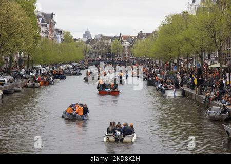 Die Niederlande feiern den Königstag nach zwei Jahren der Annullierung aufgrund der COVID-19 Coronavirus-Pandemie und der Sperrbeschränkungen und -Maßnahmen. Tausende von Einheimischen und Besuchern besuchten die Kanäle von Amsterdam, um mit verschiedenen Festlichkeiten den Geburtstag von König Willem-Alexander, bekannt als Koningsdag, zu feiern, einem niederländischen Nationalfeiertag. Alle Arten von Booten und Schiffen werden in den Kanälen gesehen, die unter den berühmten Brücken und in der Nähe der engen Häuser von Amsterdam vorbeifahren, mit Leuten, die tanzen und Spaß haben. Die Boote ziehen in den Kanälen der Innenstadt entlang, während sich Reisende auf den Straßen versammeln. Du Stockfoto