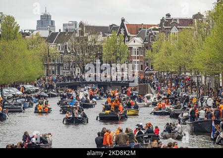 Die Niederlande feiern den Königstag nach zwei Jahren der Annullierung aufgrund der COVID-19 Coronavirus-Pandemie und der Sperrbeschränkungen und -Maßnahmen. Tausende von Einheimischen und Besuchern besuchten die Kanäle von Amsterdam, um mit verschiedenen Festlichkeiten den Geburtstag von König Willem-Alexander, bekannt als Koningsdag, zu feiern, einem niederländischen Nationalfeiertag. Alle Arten von Booten und Schiffen werden in den Kanälen gesehen, die unter den berühmten Brücken und in der Nähe der engen Häuser von Amsterdam vorbeifahren, mit Leuten, die tanzen und Spaß haben. Die Boote ziehen in den Kanälen der Innenstadt entlang, während sich Reisende auf den Straßen versammeln. Du Stockfoto