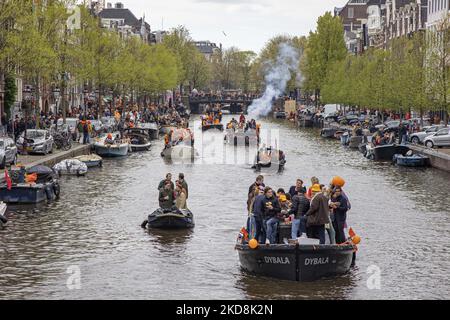 Die Niederlande feiern den Königstag nach zwei Jahren der Annullierung aufgrund der COVID-19 Coronavirus-Pandemie und der Sperrbeschränkungen und -Maßnahmen. Tausende von Einheimischen und Besuchern besuchten die Kanäle von Amsterdam, um mit verschiedenen Festlichkeiten den Geburtstag von König Willem-Alexander, bekannt als Koningsdag, zu feiern, einem niederländischen Nationalfeiertag. Alle Arten von Booten und Schiffen werden in den Kanälen gesehen, die unter den berühmten Brücken und in der Nähe der engen Häuser von Amsterdam vorbeifahren, mit Leuten, die tanzen und Spaß haben. Die Boote ziehen in den Kanälen der Innenstadt entlang, während sich Reisende auf den Straßen versammeln. Du Stockfoto