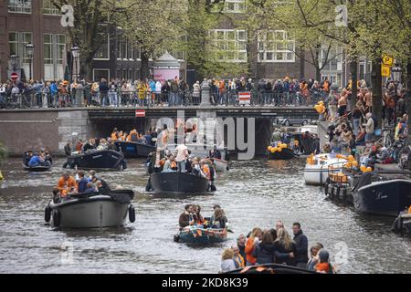 Die Niederlande feiern den Königstag nach zwei Jahren der Annullierung aufgrund der COVID-19 Coronavirus-Pandemie und der Sperrbeschränkungen und -Maßnahmen. Tausende von Einheimischen und Besuchern besuchten die Kanäle von Amsterdam, um mit verschiedenen Festlichkeiten den Geburtstag von König Willem-Alexander, bekannt als Koningsdag, zu feiern, einem niederländischen Nationalfeiertag. Alle Arten von Booten und Schiffen werden in den Kanälen gesehen, die unter den berühmten Brücken und in der Nähe der engen Häuser von Amsterdam vorbeifahren, mit Leuten, die tanzen und Spaß haben. Die Boote ziehen in den Kanälen der Innenstadt entlang, während sich Reisende auf den Straßen versammeln. Du Stockfoto