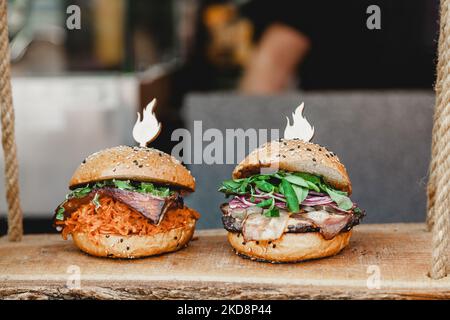 Leckere Burger auf Holzbasis. Zwei leckere hausgemachte Burger mit Rindfleisch, Käse und Gemüse auf einem alten Holztisch. Fett ungesunde Lebensmittel Nahaufnahme Stockfoto