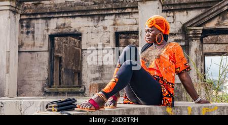 In Takoradi Ghana West Africa sitzt eine Afrikanerin in einem orangefarbenen Anzug an einer Betonwand. Stockfoto